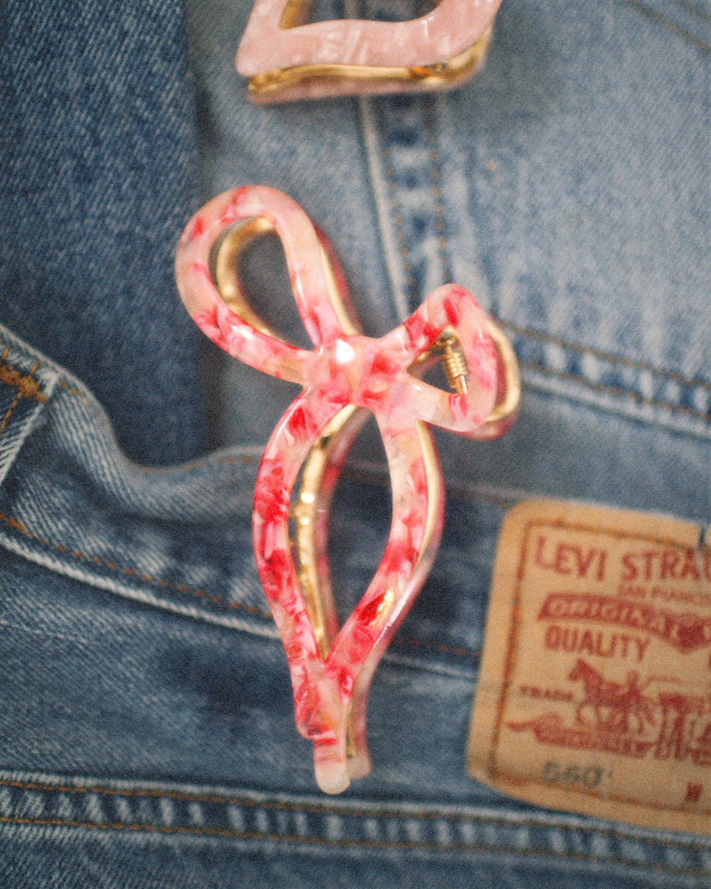 Pink bow-shaped hair clip on a Levi's denim background