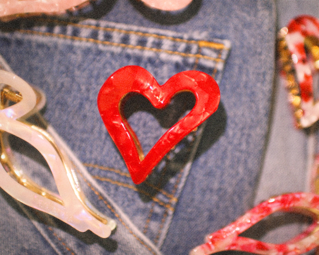 Red heart-shaped object on a denim surface with other objects around
